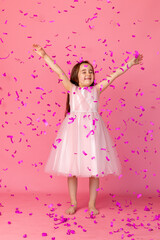 Obraz na płótnie Canvas little girl in a pink dress catches confeti smiling happy on pink background, holiday concept. A child is celebrating a birthday on a pink background