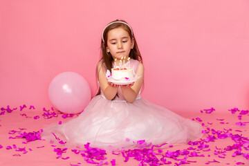 Obraz na płótnie Canvas funny little girl in a beautiful dress makes a wish and blows out the candles on the birthday cake. child celebrates his birthday. lifestyle. space for text. High quality photo