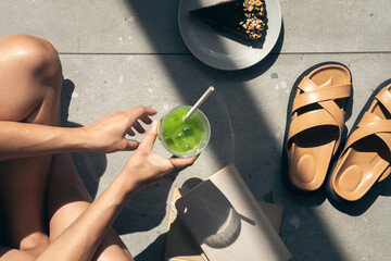 Summer composition with slippers, books, cake and lemonade in female hands.