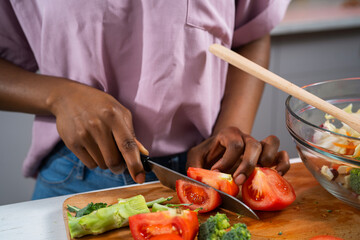 Young African woman in kitchen. Close up of woman making salad.