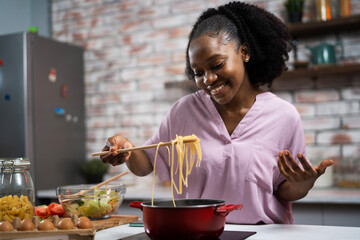 Young woman in kitchen. Beautiful African woman cooking pasta..