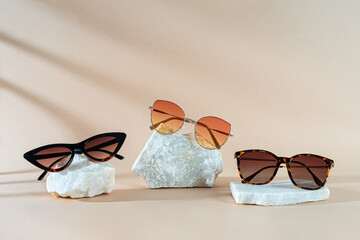 Three pairs of womens sunglasses on stones on beige background with shadows - summer eyewear fashion concept. Minimalism. Copy space for text. Sunglasses sale banner. Optic store discount, promotion - Powered by Adobe