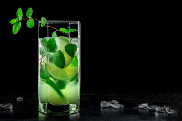 Mojito cocktail. Summer cold drink with lime, fresh mint, and ice. Cool beverage, side view on a black background with copy space