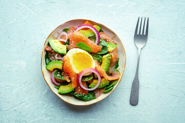 Salmon, avocado and egg salad with fresh leaves and onions, overhead flat lay shot on a slate background, with a fork. Healthy diet