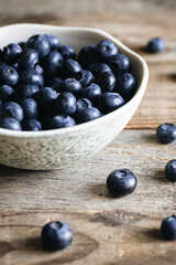 Ceramic white bowl with blueberries on a wooden background, rustic style.