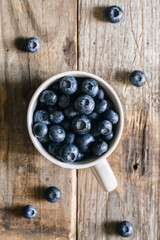 Naklejka na ściany i meble Fresh raw organic farm blueberry in white cup on rustic wooden background, top view.