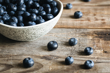 Ceramic white bowl with blueberries on a wooden background, rustic style.