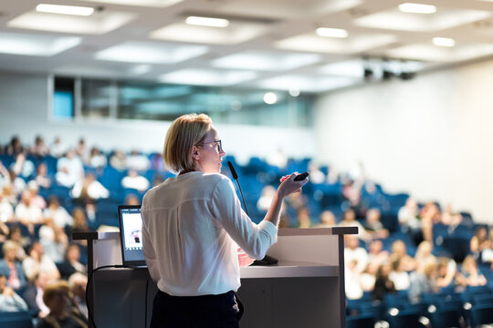 Female speaker giving a talk on corporate business conference. Unrecognizable people in audience at conference hall. Business and Entrepreneurship event