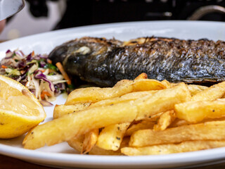 Grilled fish with lemon on plates with fried potatoes