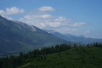 Fototapeta na wymiar zdjęcie przedstawiające krajobraz górski wysokie szczyty i doliny nad którymi jest niebieskie niebo z kłębiącymi się chmurami. Lasy w dolinach gór, krajobraz górski natura i cisza i spokój
