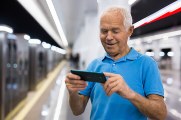 Senior man writing message on smartphone screen in subway