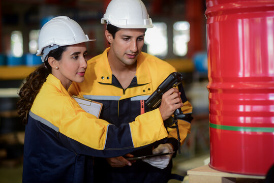 2 Latino male and female auditor wearing safety uniform workwear with handheld barcode scanner or integrated rfid handheld reader and tablet computer counts goods in warehouse of factory Manufacture.