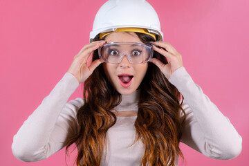 Portrait of emotional and surprised young architect wearing protective goggles on the pink background. 