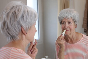 Senior woman moisturizing her lips in the bathroom