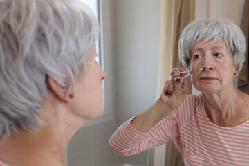 A senior woman in her sixties is using some small scissors to cut her nose hairs