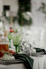 Beautiful table setting. On the plate lies a green napkin, a bag with sweet desserts of white and green color. A fork, knife and glasses are on the side. Side view.