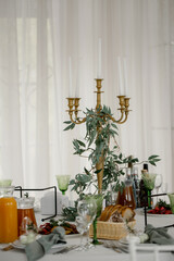 A beautifully set table, on the table there is a candlestick decorated with plants, glasses, pasud and drinks.