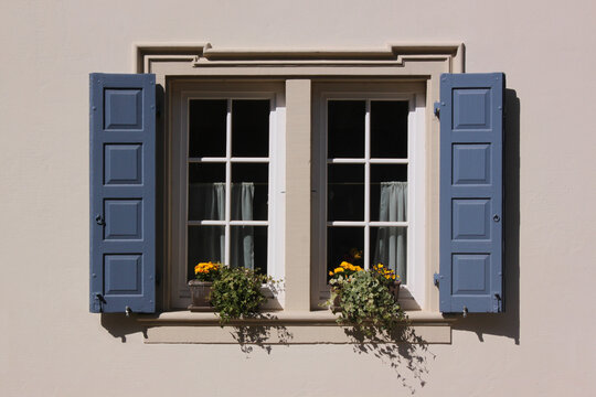 White baroque window with flower pot and blue shutters on a residential house in the old village of Neu-Bamberg, Germany
