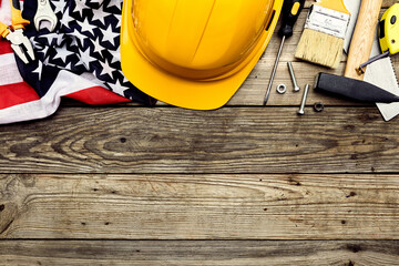 Safety helmet, American flag with construction tools on wooden background. Happy Labor day banner template.