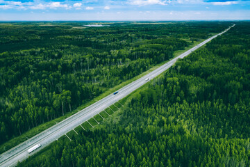 Aerial view of highway road with cargo transport and cars through green woods