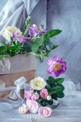 Bouquet of fresh roses in pastel shades, in craft paper packaging, against a gray concrete wall and silk fabric, still life 