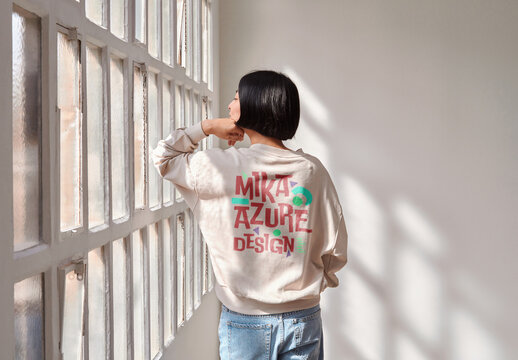 Mockup of Japanese woman wearing customizable long sleeve top leaning on window, rear view