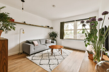 a living room with wood flooring and white walls, plants in vases on the side of the couch