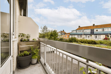 a balcony with potted plants on the railings and houses in the background, taken from an apartment window