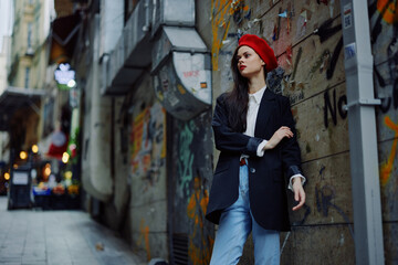 Obraz na płótnie Canvas Fashion woman portrait walking tourist in stylish clothes with red lips walking down a narrow city street, travel, cinematic color, retro vintage style, dramatic against a wall with graffiti.