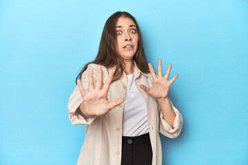 Stylish young woman in an overshirt on a blue background being shocked due to an imminent danger