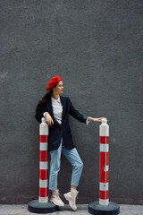 Fashion woman standing on the street in front of the city and road works tourist in stylish clothes with red lips and red beret, travel, cinematic color, retro vintage style.