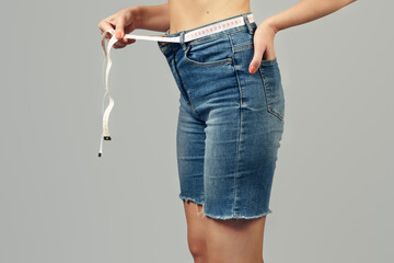 Weight loss concept. The girl holds a measuring tape wrapped around her waist instead of a belt on...