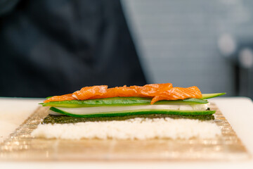 Close-up of a sushi maker in black gloves preparing sushi using rice nori sheets salmon fillet curd...