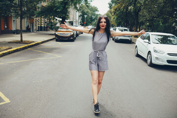 Fototapeta premium A happy girl walks down the street along the roadway with her arms outstretched and smiling.
