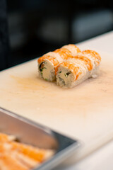 Close-up of a sushi man in black gloves cutting a california roll on a white kitchen board in a professional kitchen 
