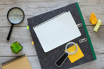 open notebook and other office equipment such as magnifier, notepad, stickers on wooden office table.