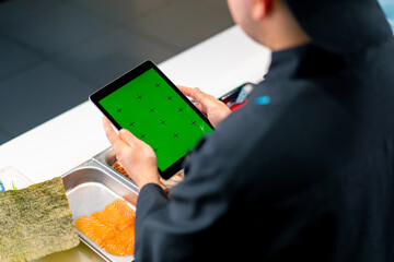 Close-up from behind the sushi chef holding a tablet with a green screen open while making sushi...