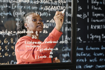 African American teacher writing codes on blackboard, she teaching IT lesson at school - Powered by Adobe