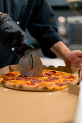 man pizza chef cuts pizza lying in a delivery box with a pizza knife in the kitchen of a pizzeria 