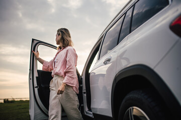 Young woman going out of car, walking in nature.
