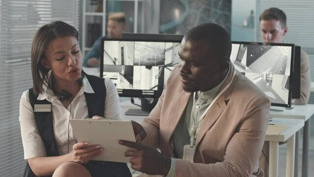 Waist up slowmo of diverse couple of security agency managers discussing paper documents at workplace in contemporary office