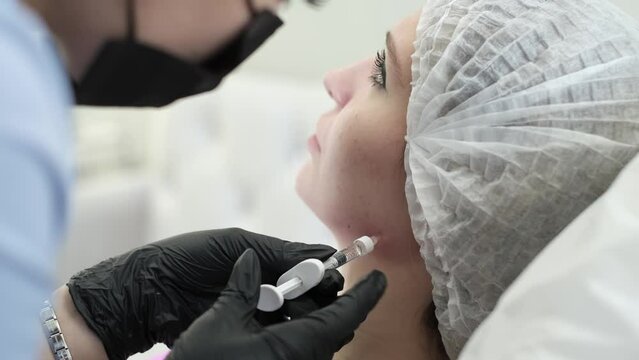 With syringe in hand, beauty doctor is shown performing injection into the patient's jowls, part of effective treatment sculpt facial contour. patient lying during non-surgical face lift procedure