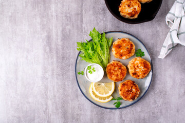 Cutlets with codfish and shrimps served with salad leaves, lemon and sour cream sauce on the plate on gray table. Top view. Copy space