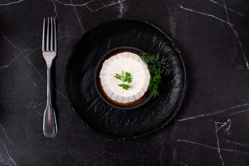 Fresh ricotta cheese topped with parsley on black plate and fork on dark table. Top view