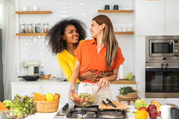 Diversity young happy love LGBT, LGBTQ caucasian and african family lesbian couple woman cook vegan food healthy eat with fresh vegetable salad in kitchen at home, pride, rainbow.Lgbt lesbian couple