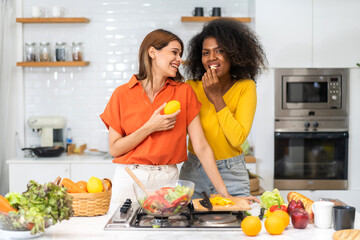 Diversity young happy love LGBT, LGBTQ caucasian and african family lesbian couple woman cook vegan food healthy eat with fresh vegetable salad in kitchen at home, pride, rainbow.Lgbt lesbian couple