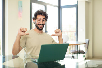 young adult bearded man with a laptop feeling proud, arrogant and confident, looking satisfied and...