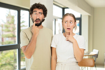 young adult couple with surprised, nervous, worried or frightened look, looking to the side towards...