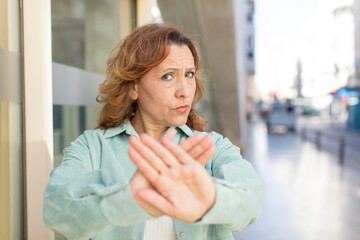 middle age woman covering face with hand and putting other hand up front to stop camera, refusing...