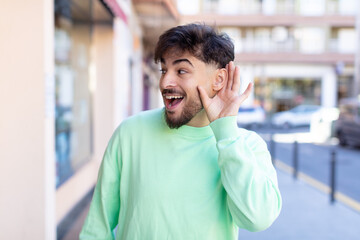 young handsome man looking happy, listening, trying to hear a secret conversation or gossip,...